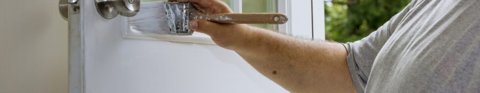 male worker using a paint brush to paint a white external wooden door